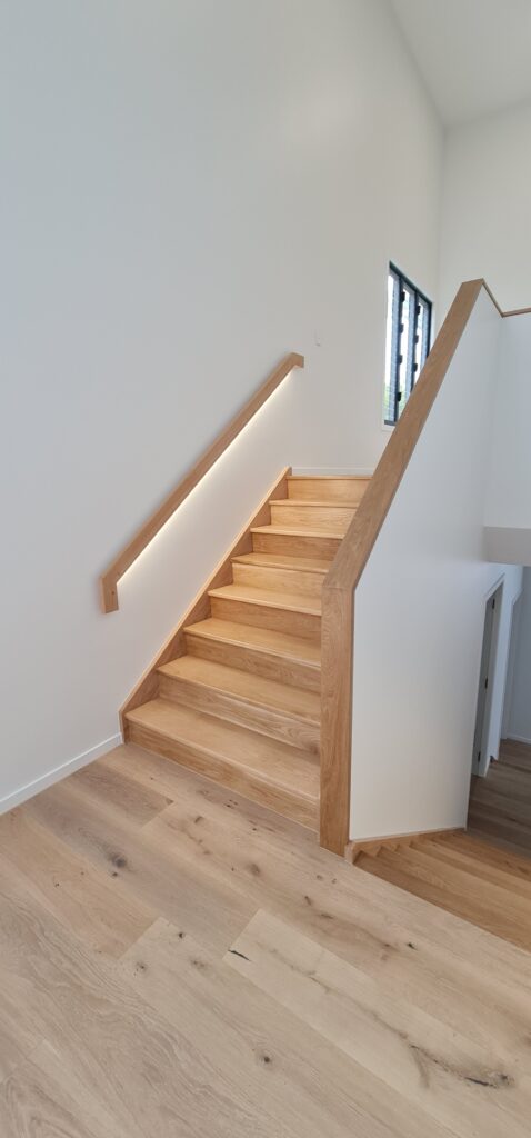Stair with LED wall rail and timber capping over a half wall.