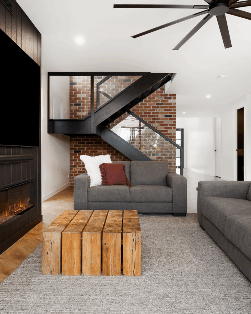 Image of timber stair with glass balustrade in background against a brick wall with loungeroom furniture in the foreground
