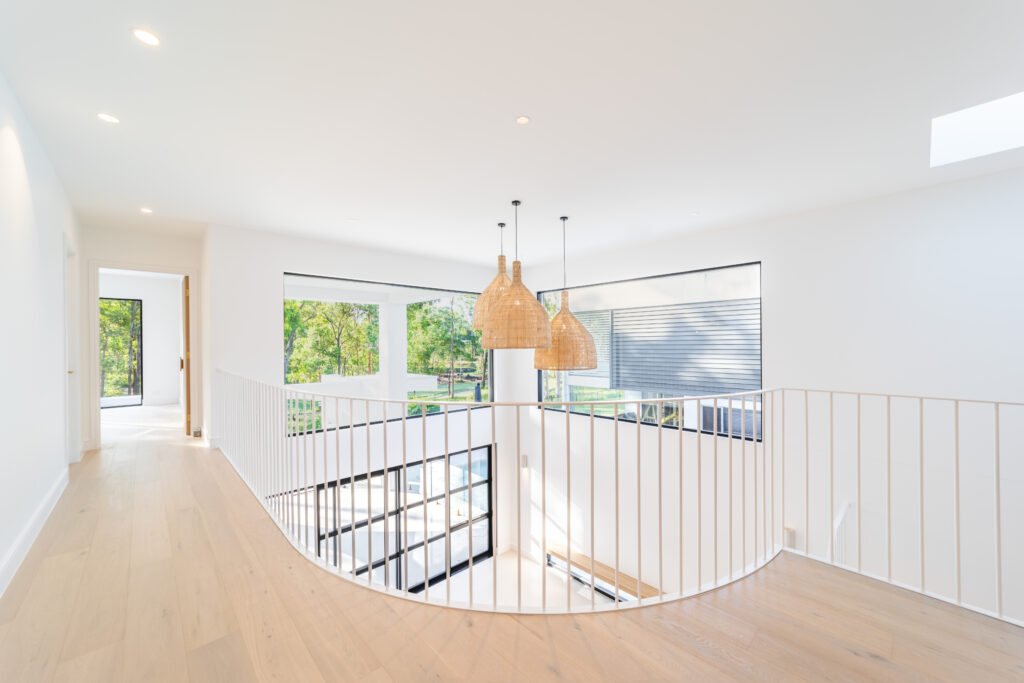View of upstairs hallway with powdercoated balustrade along one side, light fittings and windows in the background