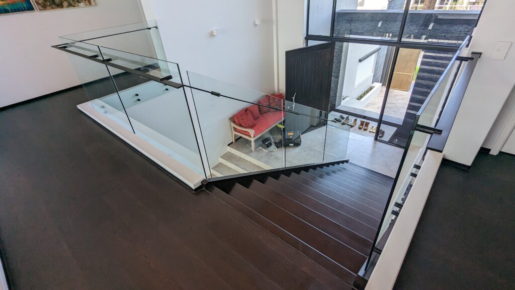 Looking down over stair with frameless glass balustrade. A couch is in the background