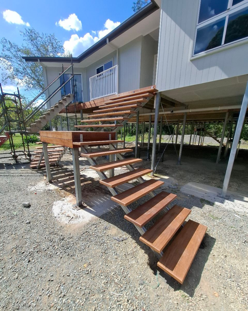 External stair with two lower flights meeting at an elevated landing platform with a single top flight. A view of the On The Way Up van is in the background