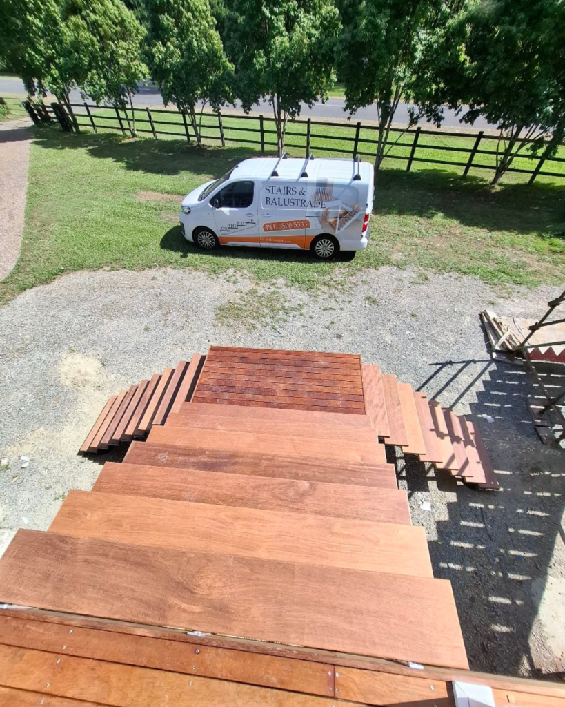 External stair with two lower flights meeting at an elevated landing platform with a single top flight. A view of the On The Way Up van is in the background