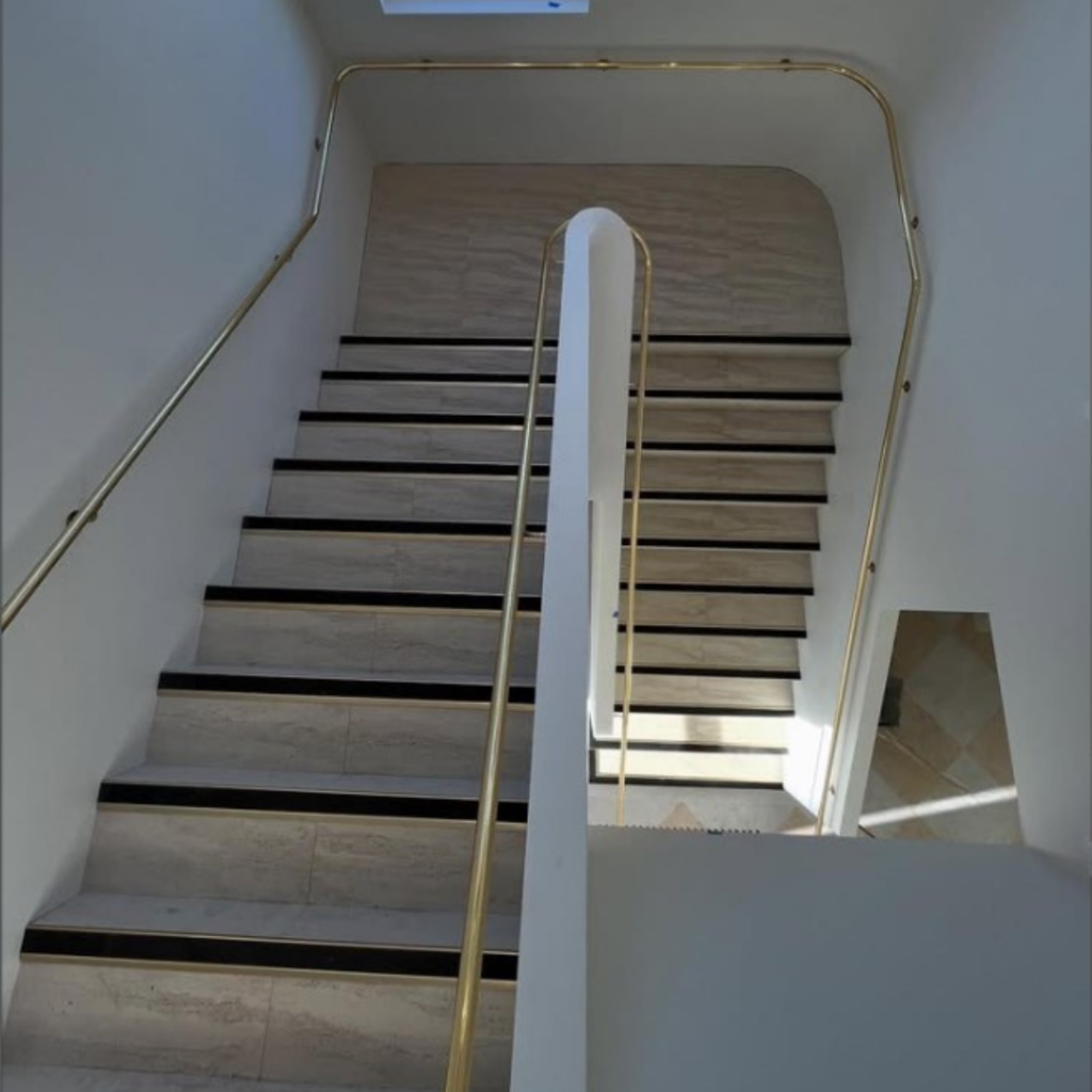 Polished brass handrail on both sides of concrete stair curved around the landing