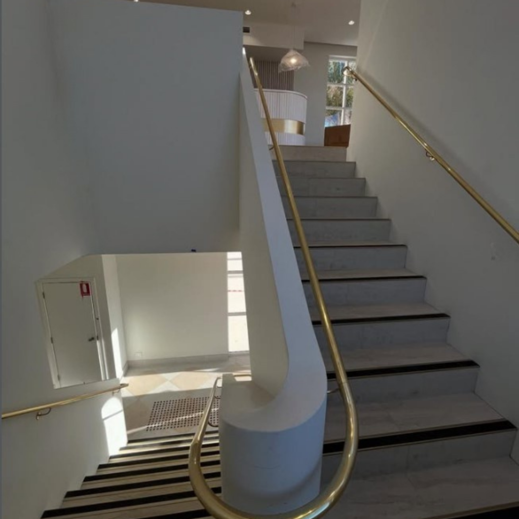 Polished brass handrail on both sides of concrete stair curved around the landing